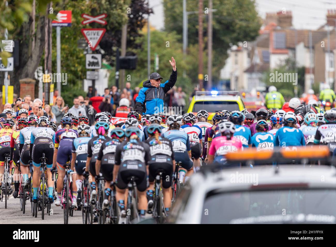 Direttore di gara che guida i piloti attraverso la partenza neutralizzata alla gara ciclistica AJ Bell Women's Tour a Shoeburyness, Essex, Regno Unito. Seguono le auto di supporto Foto Stock