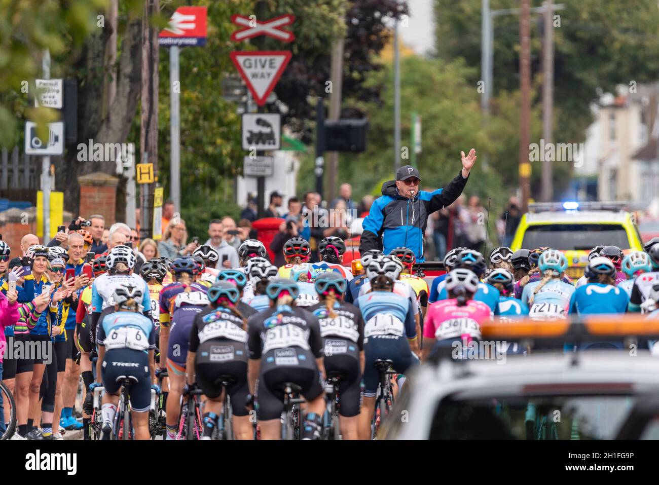 Direttore di gara che guida i piloti attraverso la partenza neutralizzata alla gara ciclistica AJ Bell Women's Tour a Shoeburyness, Essex, Regno Unito. Seguono le auto di supporto Foto Stock
