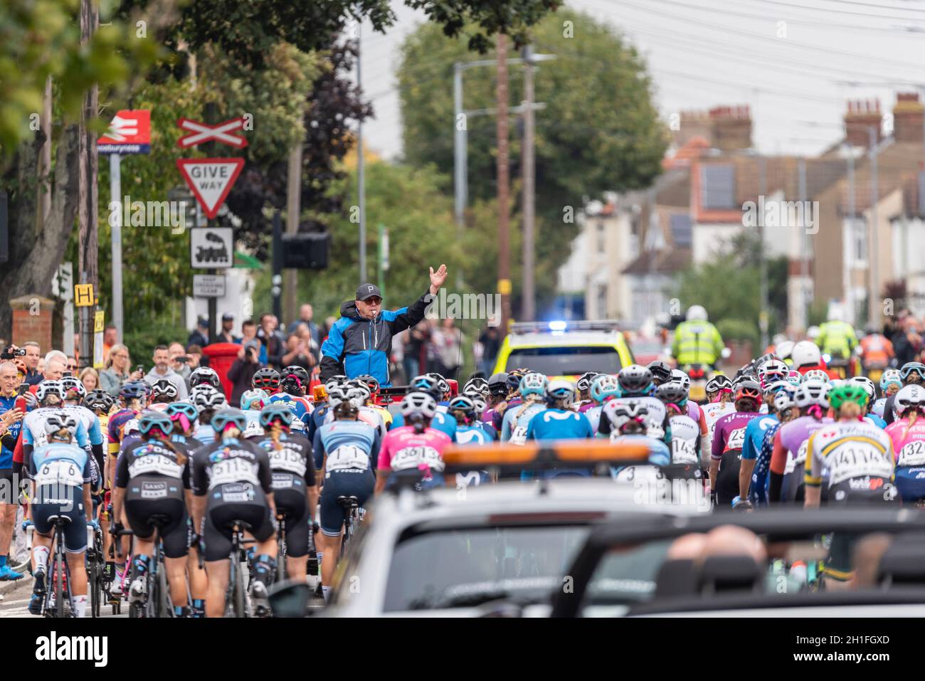Direttore di gara che guida i piloti attraverso la partenza neutralizzata alla gara ciclistica AJ Bell Women's Tour a Shoeburyness, Essex, Regno Unito. Seguono le auto di supporto Foto Stock