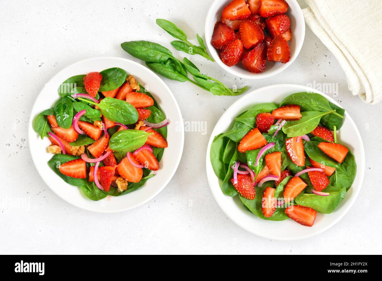 Macedonia di frutta con fragola e spinaci in ciotola bianca su sfondo chiaro. Colazione sana. Vista dall'alto, piatto Foto Stock