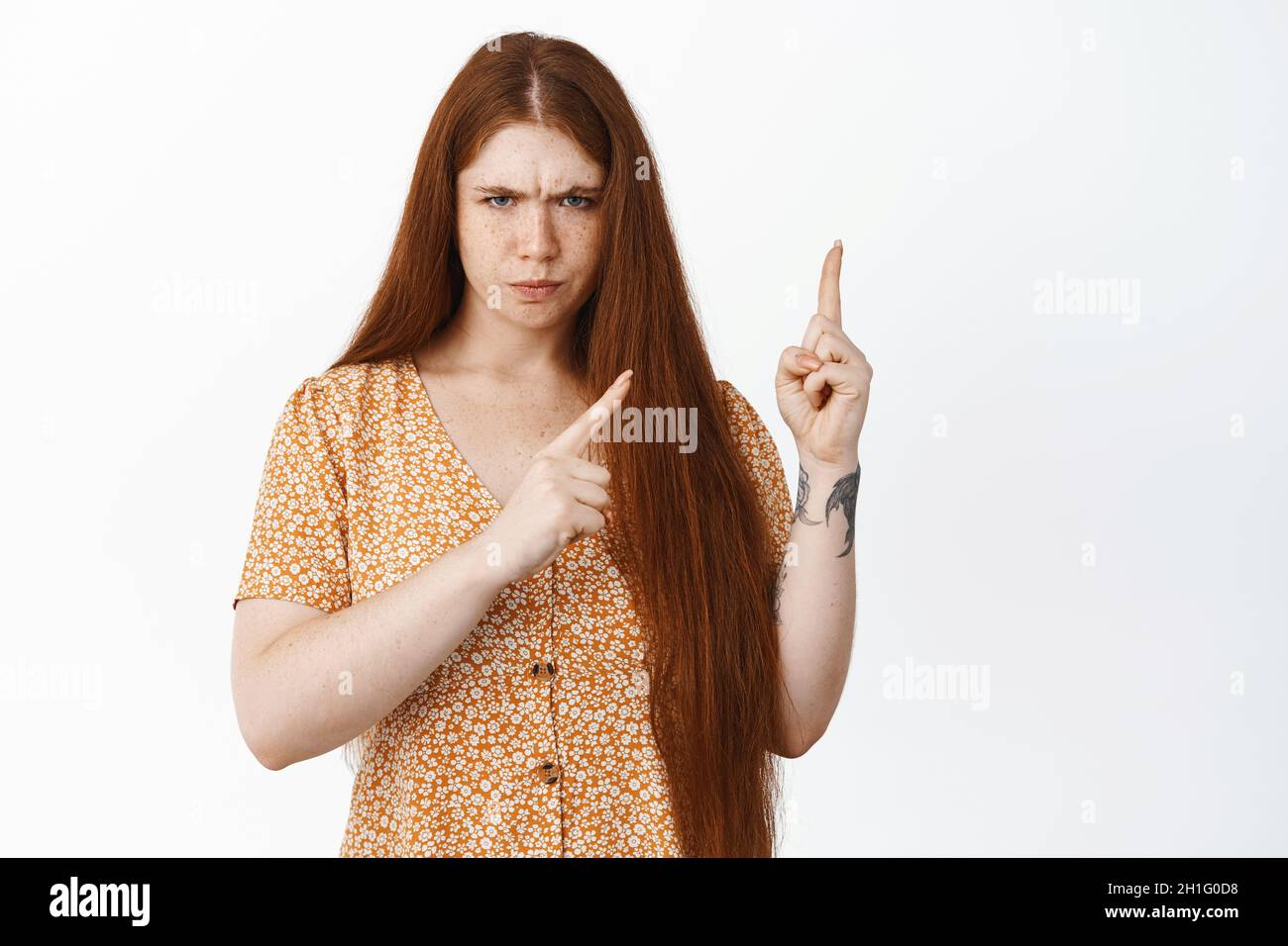 Immagine di giovane ragazza redhead arrabbiata che punta in alto a destra angolo, sembra dispiaciuto e deluso, lamentarsi o condannare cattivo, bianco Foto Stock