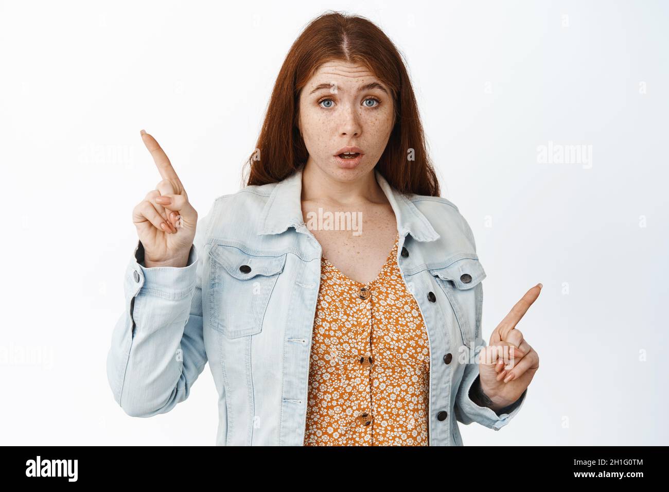 La giovane donna confusa punta lateralmente, mostrando sinistra e destra, due opzioni, bisogno di consigli, aiuto con la scelta, in piedi su sfondo bianco Foto Stock