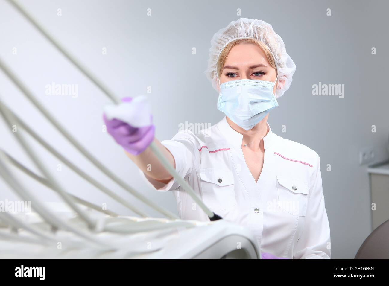 Un infermiere in uniforme e indossando una maschera medica pulisce l'apparecchiatura dentale. Disinfezione nell'ufficio odontoiatrico. Spazio di copia. Foto Stock