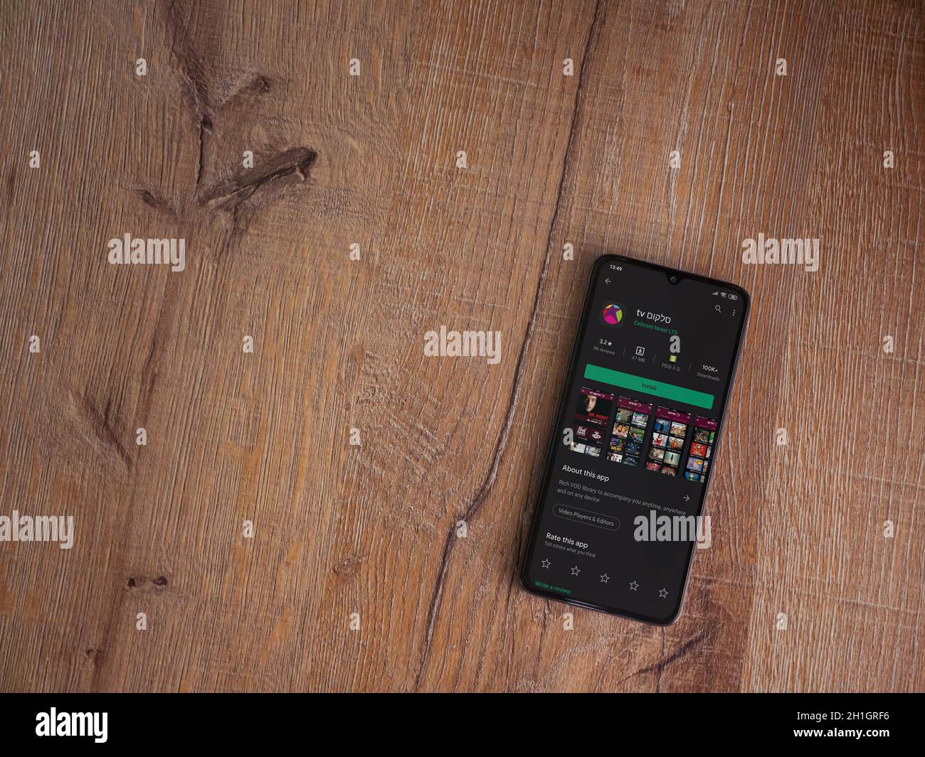 LOD, Israele - 8 luglio 2020: L'app di Cellcom TV gioca la pagina del negozio sul display di uno smartphone nero su sfondo di legno. Vista dall'alto piatto con co Foto Stock