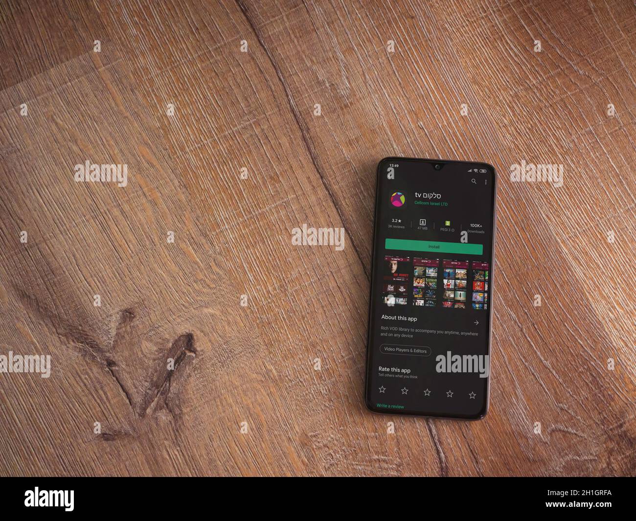 LOD, Israele - 8 luglio 2020: L'app di Cellcom TV gioca la pagina del negozio sul display di uno smartphone nero su sfondo di legno. Vista dall'alto piatto con co Foto Stock