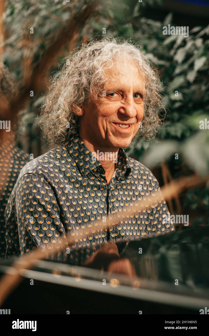 attraente flirtatiously sorridente uomo 65 anni grigio ricci capelli gioca pianoforte grande e guarda la macchina fotografica con sorriso. Persone reali, foto Foto Stock