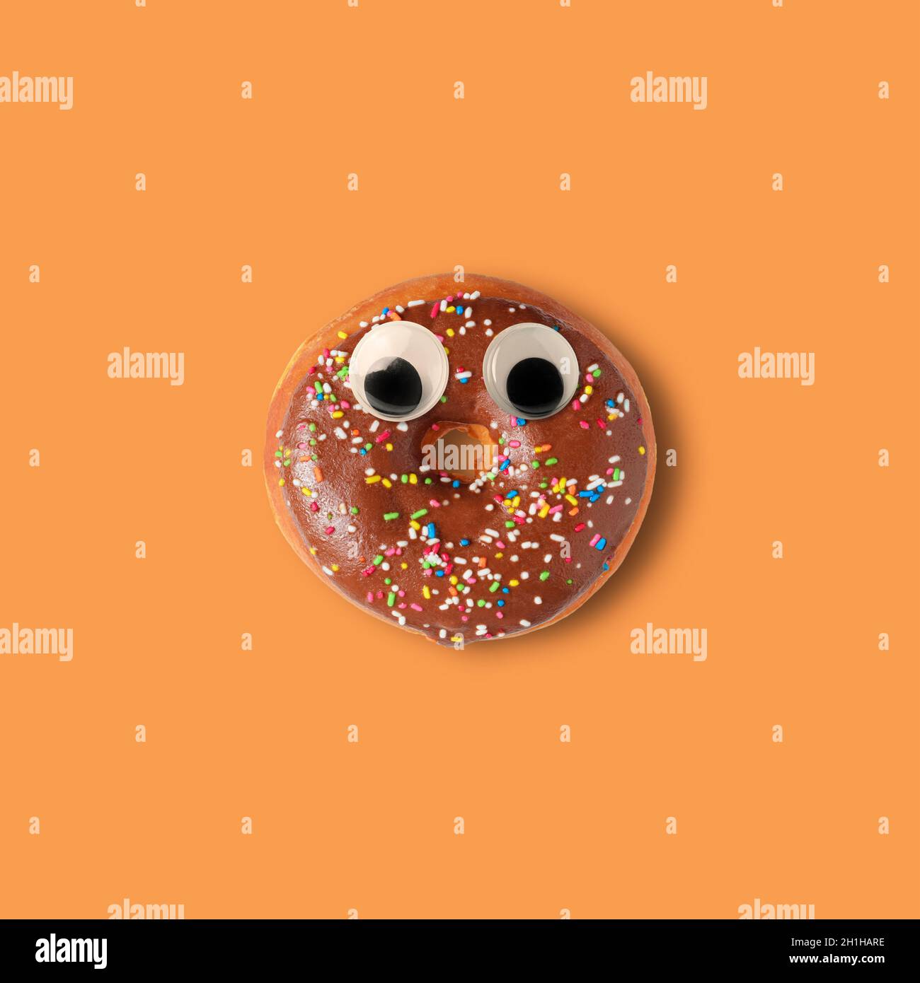 Ciambella di Halloween con occhi di googly su sfondo arancione. Divertente concetto minimo. Foto Stock