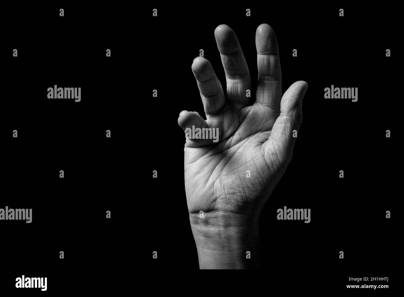 Immagine in bianco e nero di mano maschile rugosa sollevata gesturing per assistenza o in saluto, con palmo aperto fuori, isolato su uno sfondo nero con Foto Stock