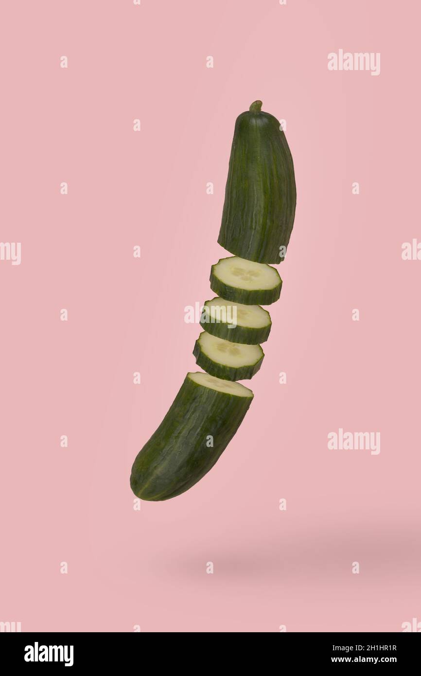 Idea minimale con cetriolo fresco affettato che galleggia in aria isolato su sfondo rosa pastello. Dieta, vitamine, vegano e cibo sano. Cibo minimo o ve Foto Stock