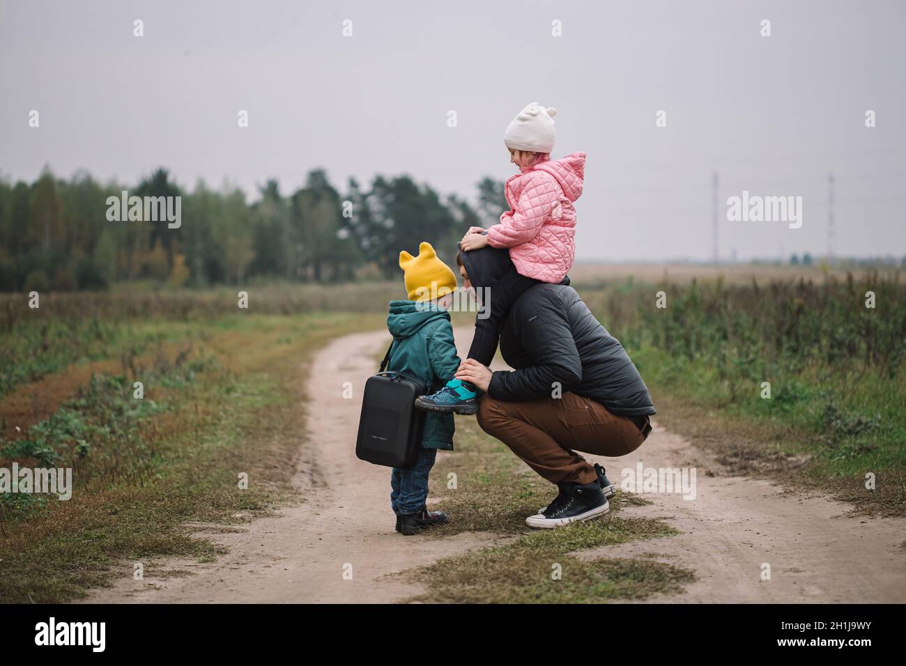 Felice famiglia con due bambini che camminano nel campo autunno tempo. Papà porta la figlia sulle spalle. Foto Stock