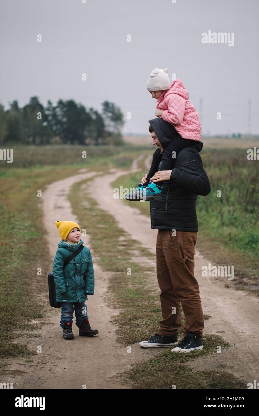 Felice famiglia con due bambini che camminano nel campo autunno tempo. Papà porta la figlia sulle spalle. Foto Stock