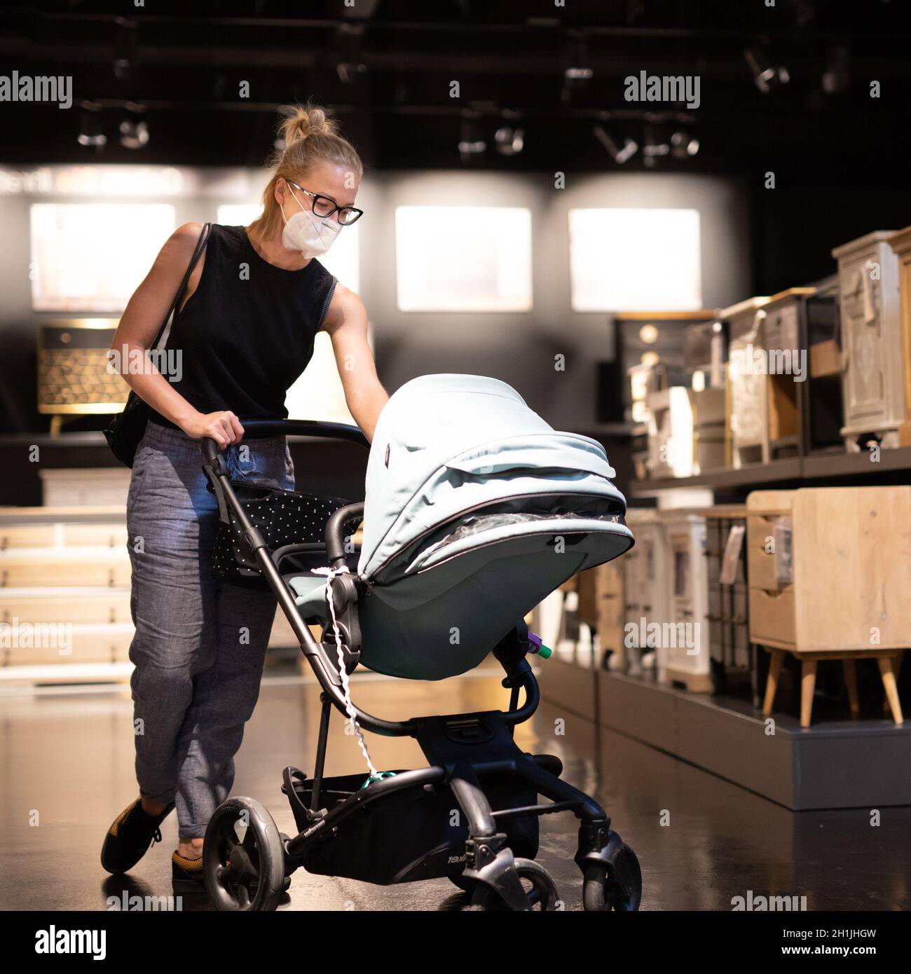 Mamma giovane con neonato in passeggino shopping al negozio di mobili e accessori casa negozio indossare maschera medica protettiva viso per prevenire la diffusione o Foto Stock