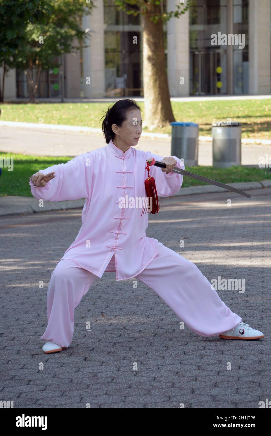 Una donna aggraziata di mezza età fa Tai Chi con una spada. Nel Flushing Meadows Corona Park a Queens, New York City. Foto Stock