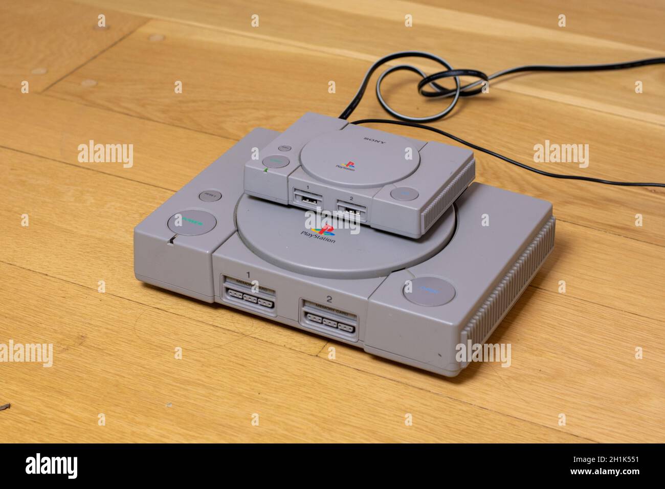 Un classico Playstion in cima a una PlayStation originale, un confronto dei due, su un pavimento in legno. Foto Stock