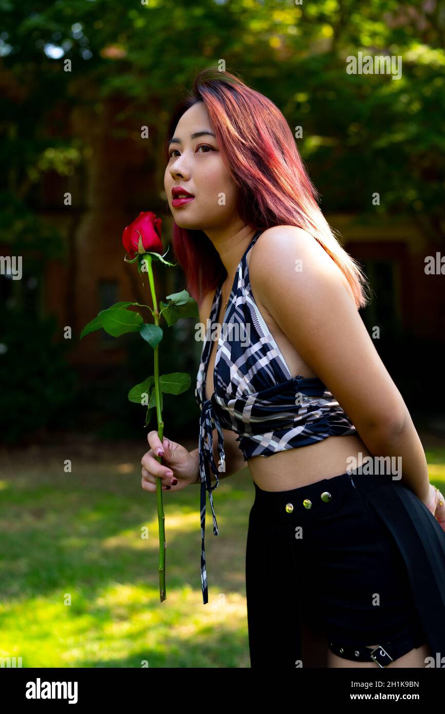 Giovane donna asiatica che tiene una rosa in un giardino impostazione Foto Stock