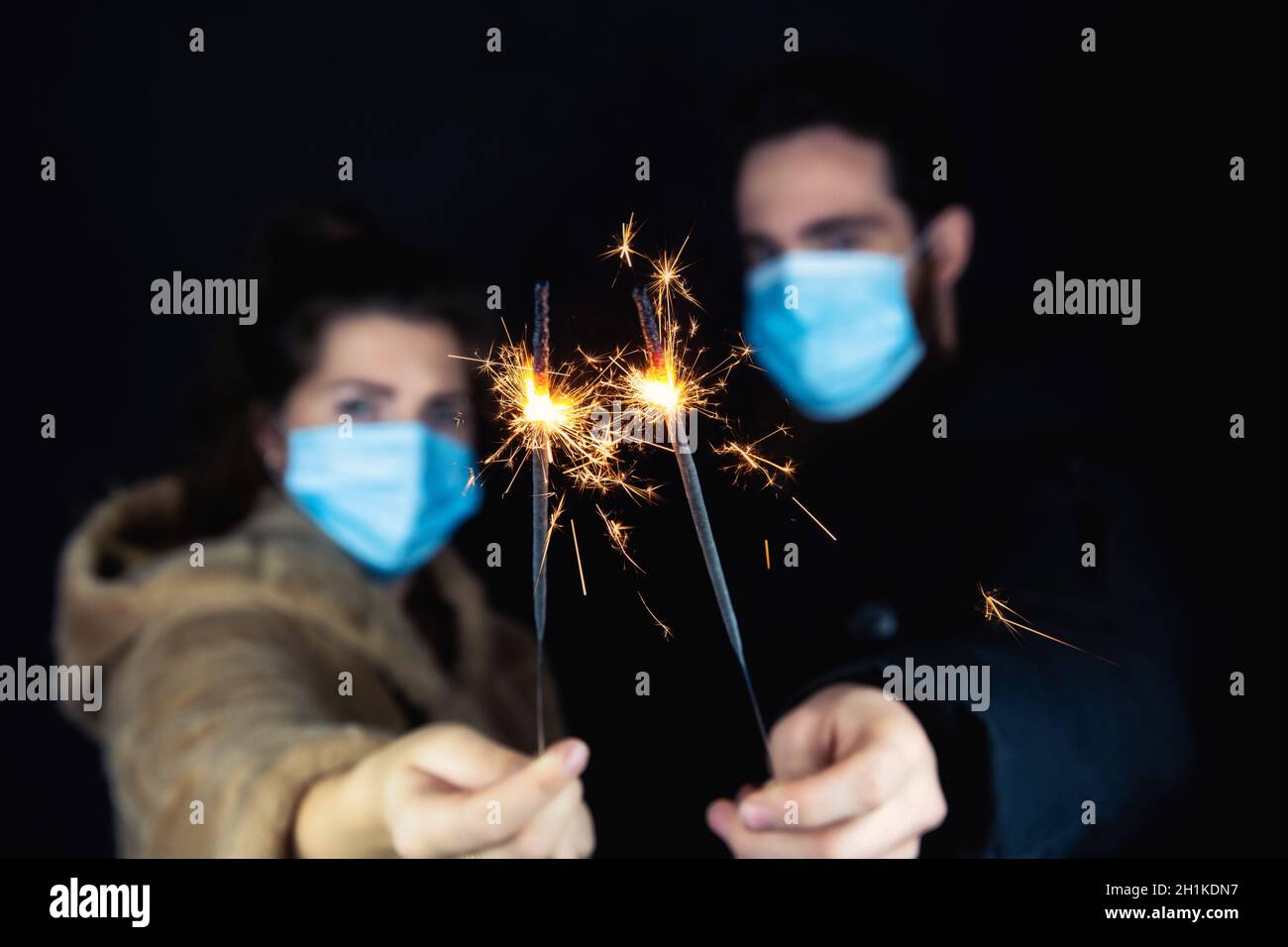 Giovane coppia che indossa maschere di protezione per Coronavirus e che tiene sparklers per Capodanno, 2021 e Covid-19 Concept Foto Stock
