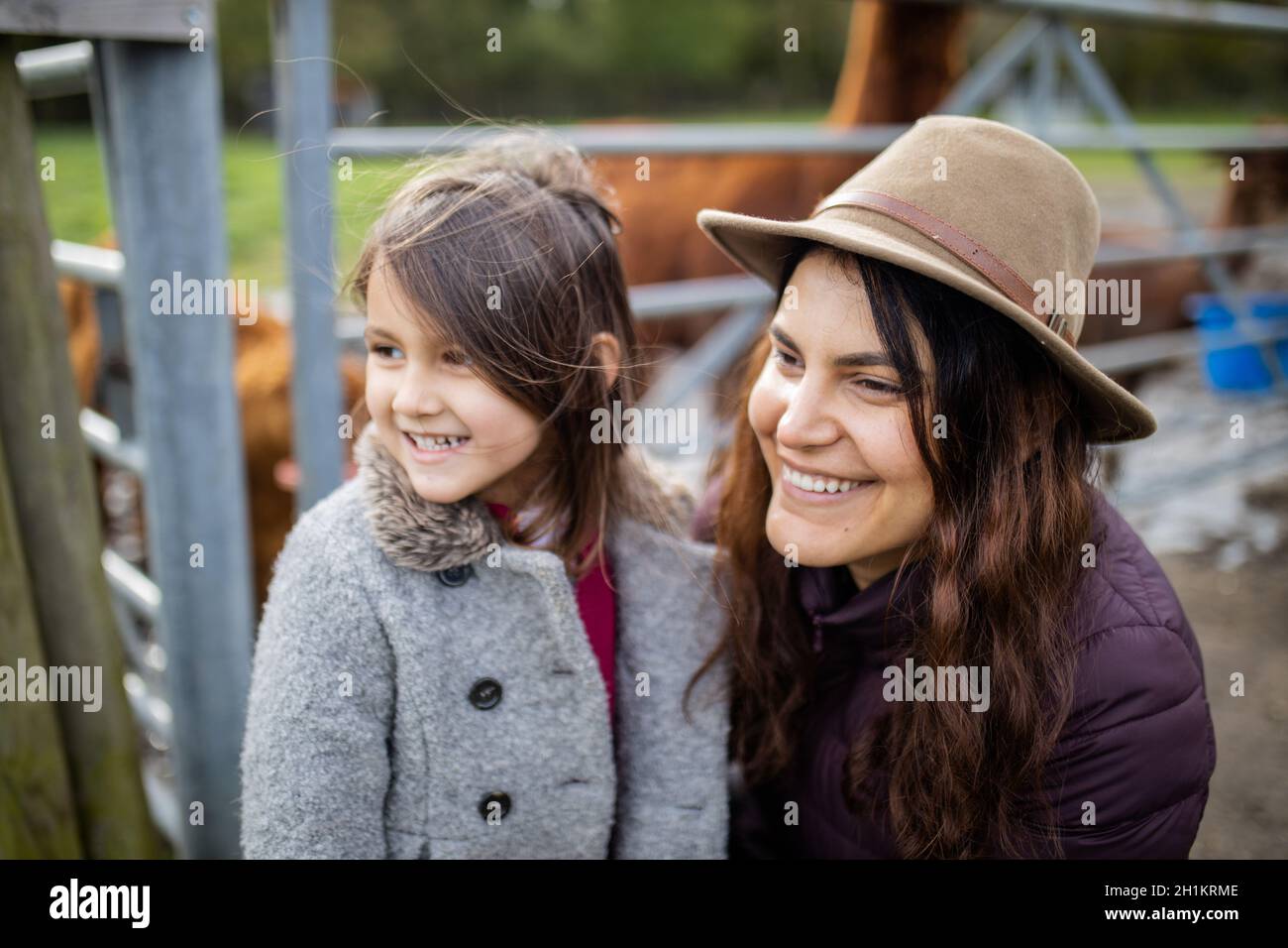 Felice donna bruna e sua figlia sorridente e guardando la distanza, mentre alpaca marrone mangiare dietro di loro Foto Stock