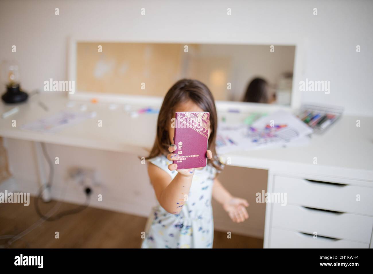 Immagina una bambina di brunette che tiene un passaporto svedese davanti al suo volto, con uno specchio e immagini colorate e matite colorate sulla parte superiore di una W. Foto Stock