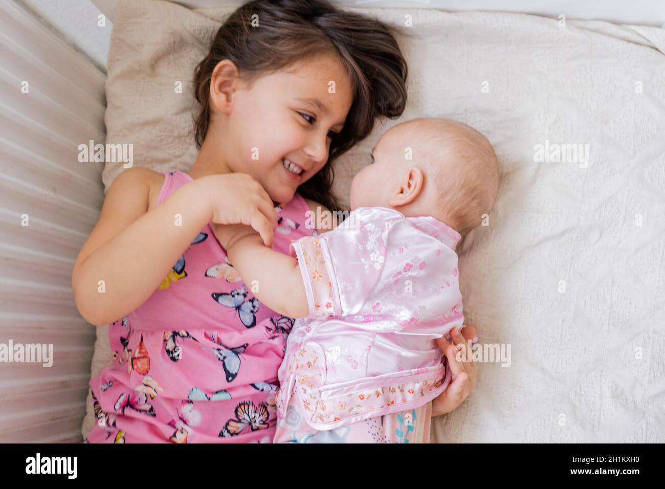 Sorelline felici in abbigliamento rosa sdraiati a letto e sorridenti l'una all'altra. Due belle sorelle in abbigliamento rosa adagiate sul letto. Fratelli giovani Foto Stock