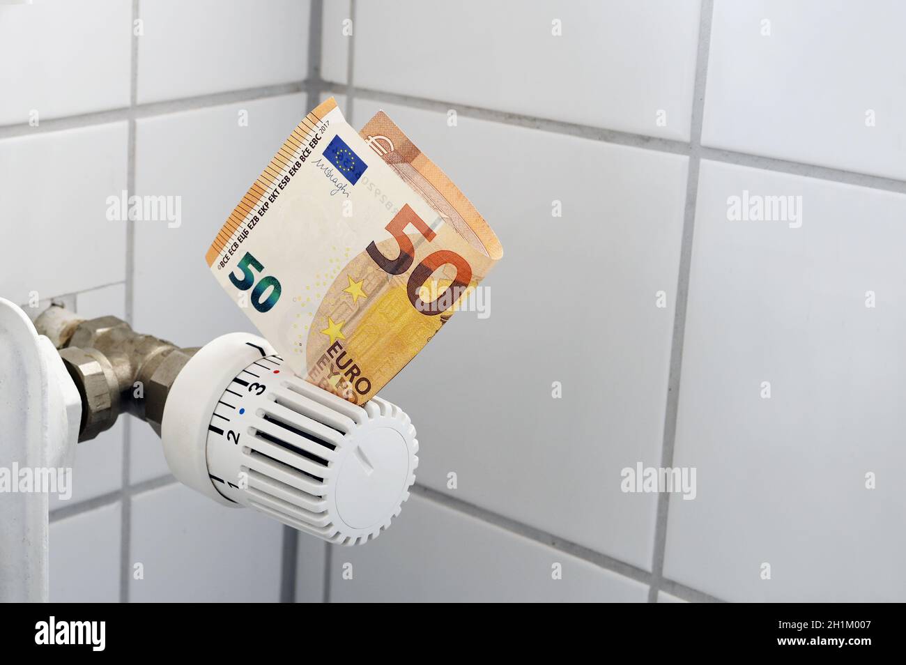 Banconote in euro bloccate nel termostato di un radiatore di riscaldamento, costi crescenti per calore ed energia, finanza domestica e concetto di denaro, spazio copia, selezionato f Foto Stock