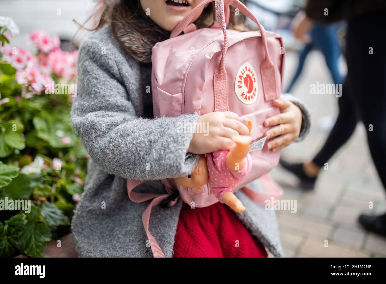 Londra, UK - 4 novembre 2020: Piccola ragazza felice con i fiori dietro il suo zaino rosa abbracciante Fjallraven e bambola piccola. Bambino giovane che tiene ruc rosa Foto Stock