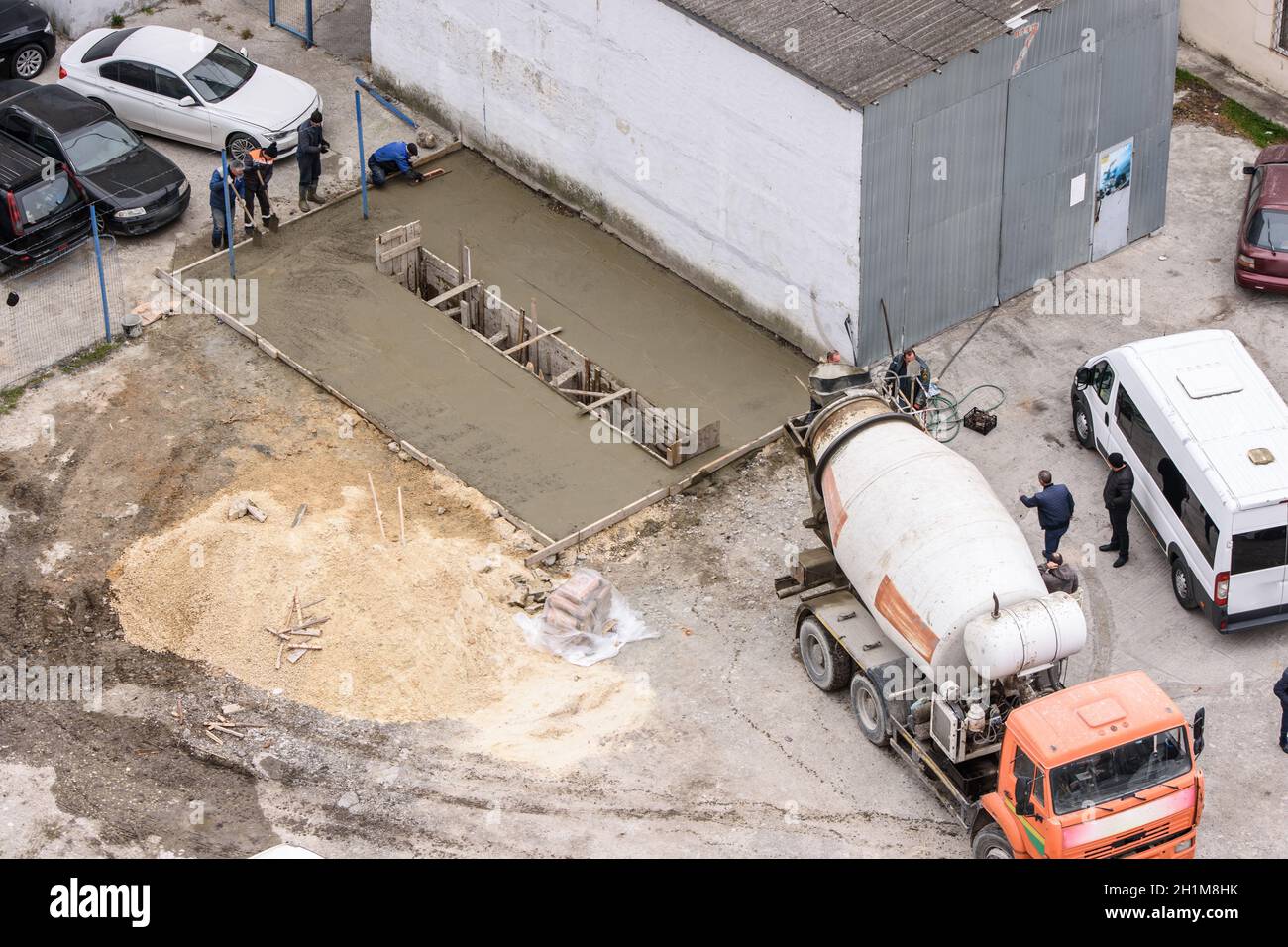 Anapa, Russia - 23 marzo 2020: Lavoratori che livellano il calcestruzzo da una betoniera per costruire una buca di ispezione dell'automobile Foto Stock