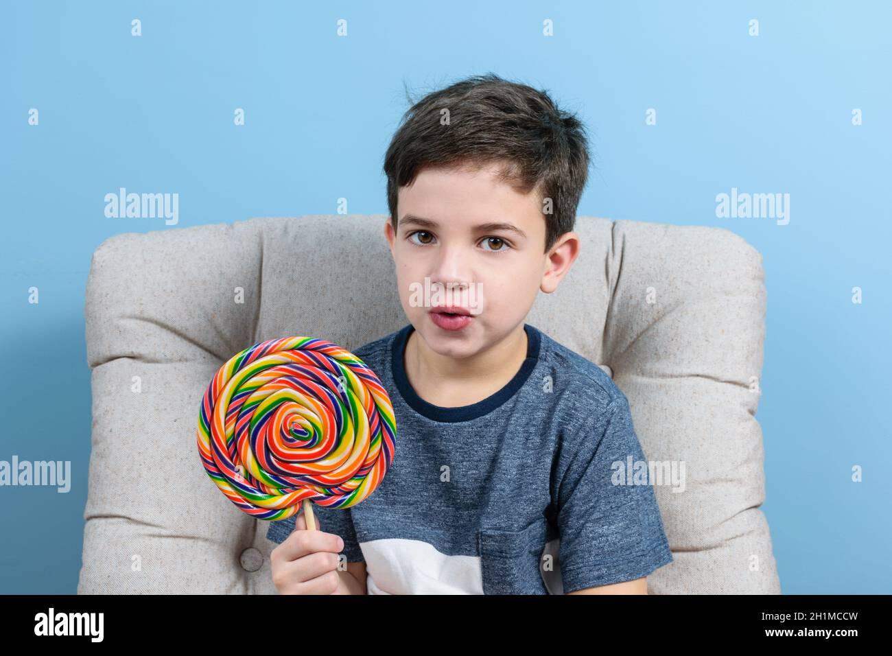 bambino di 8 anni che guarda la macchina fotografica con la bocca aperta e tenendo un grande lollipop colorato. Foto Stock