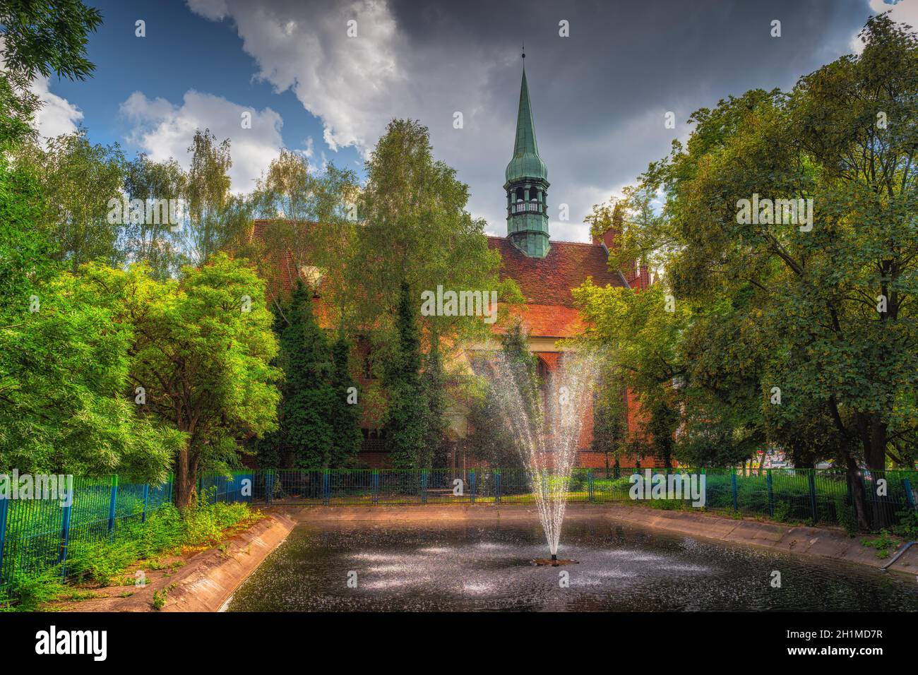 Fontana in piccolo stagno circondato da alberi verdi e Chiesa dei santi. Pietro e Paolo sullo sfondo, Szczecin, Polonia. Tecnica dell'immagine con messa a fuoco morbida Foto Stock