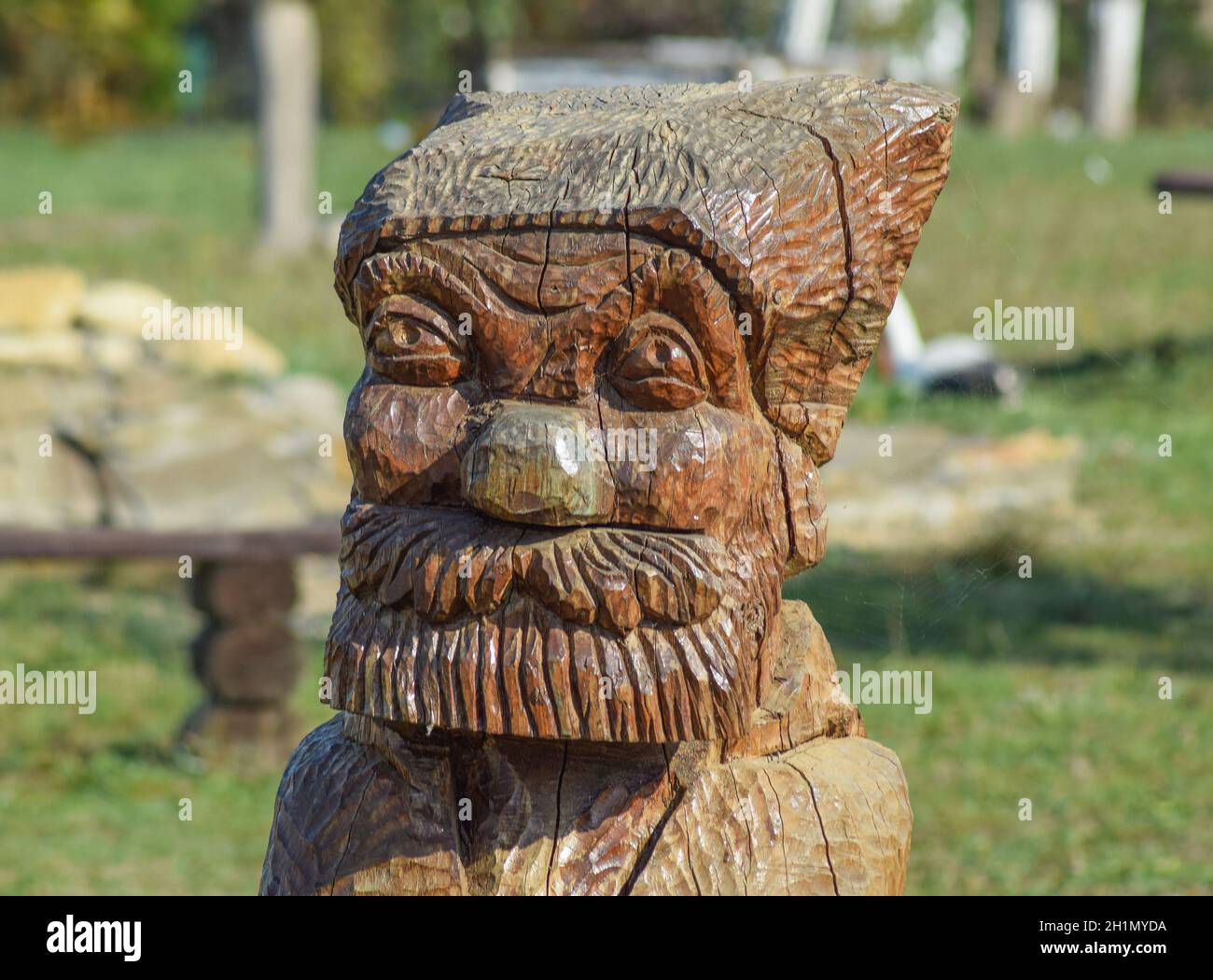 La faccia di un barbuto vecchio scolpita al di fuori del log. Idolo in legno. Foto Stock