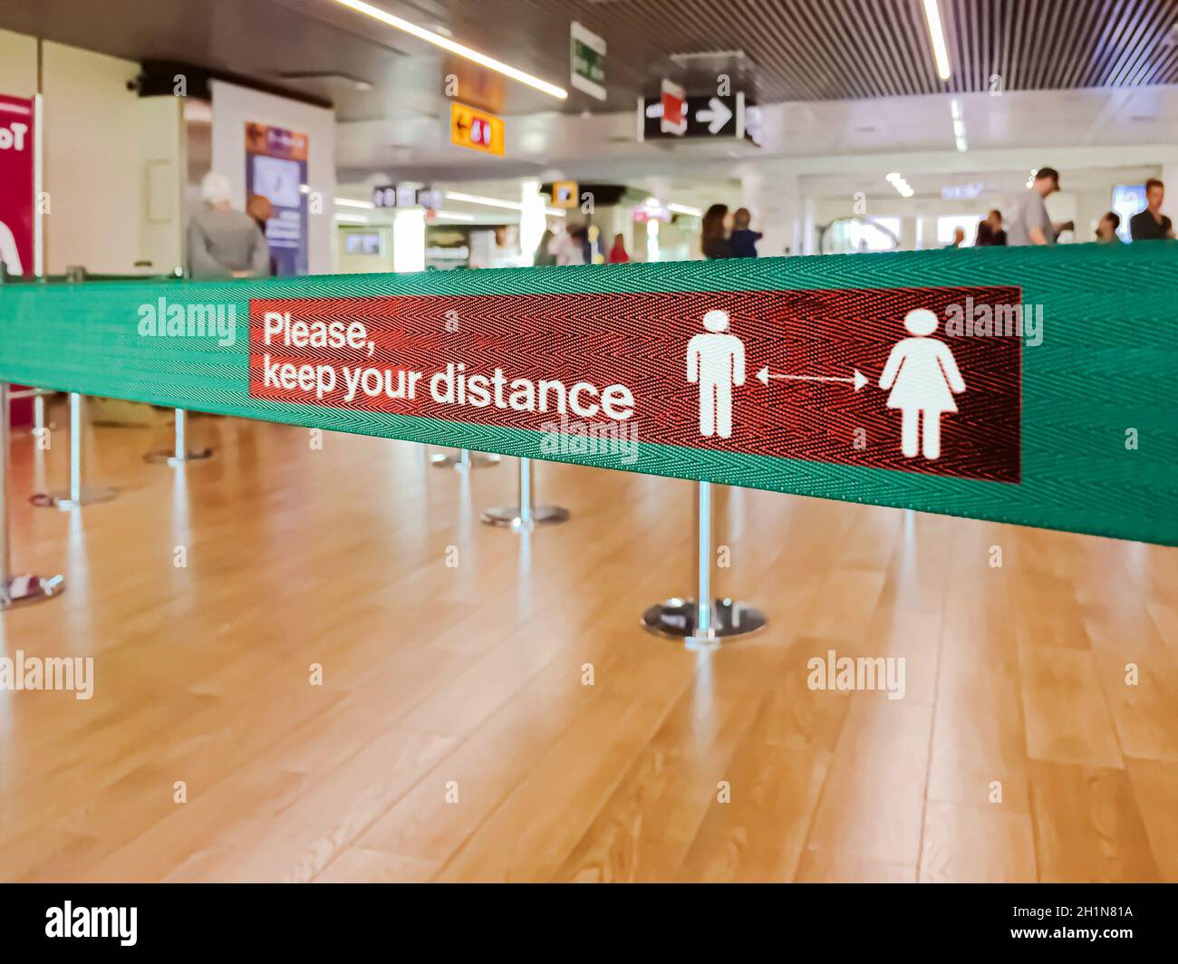 Barriera verde a nastro all'interno di un aeroporto con l'avvertimento di mantenere le distanze sociali a causa della pandemia di Coronavirus Foto Stock