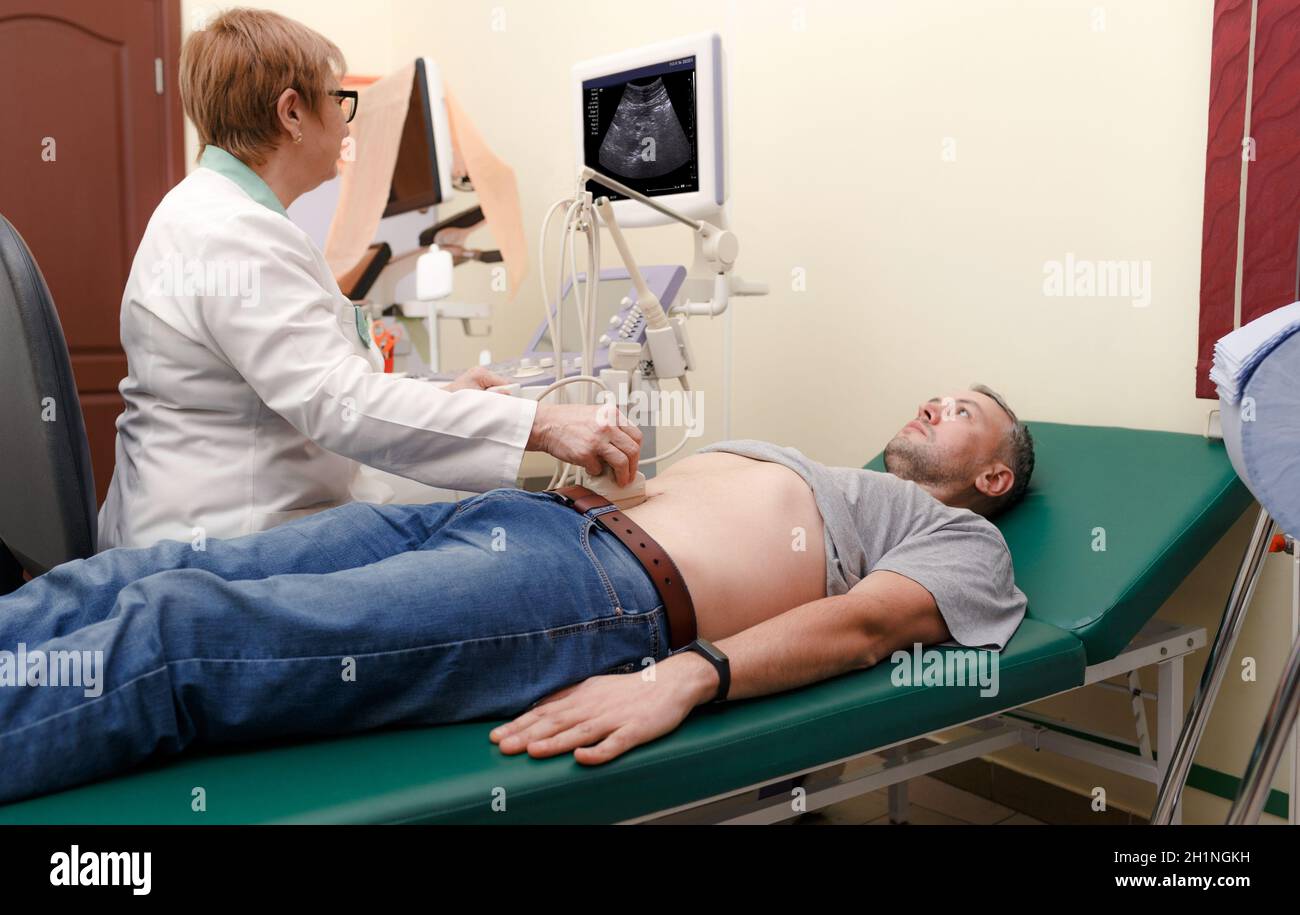 Diagnosi ecografica dello stomaco sulla cavità addominale di un uomo in clinica, primo piano. Il medico esegue un sensore a ultrasuoni sul paziente Foto Stock