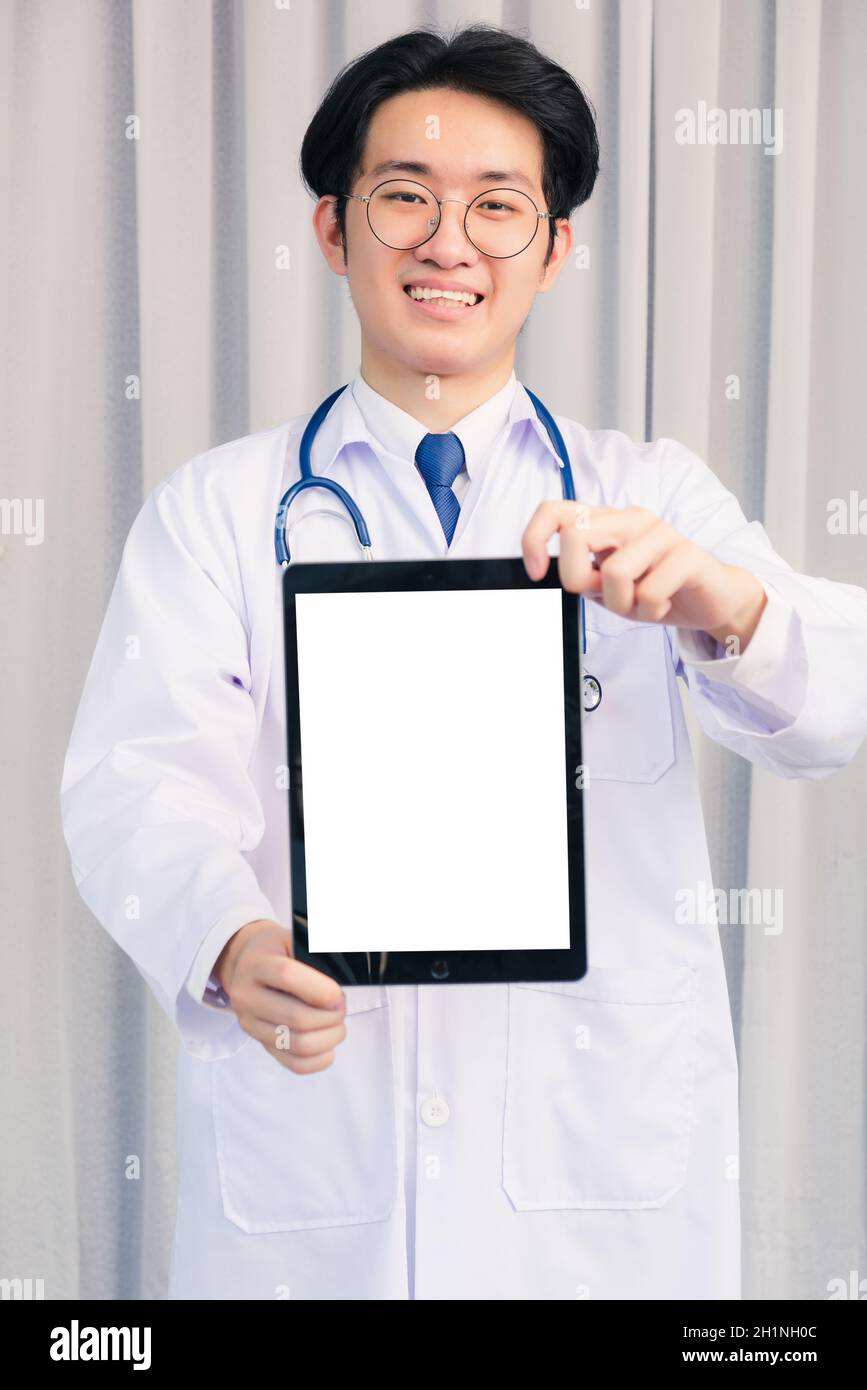 Ritratto closeup di felice asiatico giovane medico bel ragazzo sorridente in uniforme e stetoscopio tracolla che mostra schermo bianco anteriore smart tavolo digitale Foto Stock