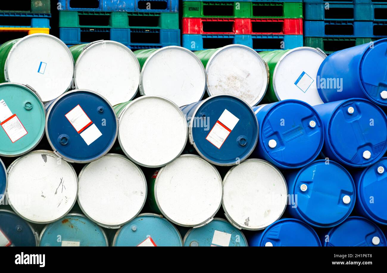 Vecchi barili chimici davanti al pallet di plastica impilato in fabbrica. Tamburo dell'olio blu e verde. Serbatoio dell'olio in acciaio e plastica. Magazzino dei rifiuti tossici. Ha Foto Stock