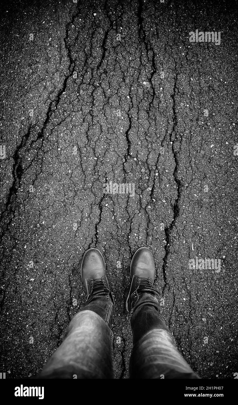Piedi dell'uomo con stivali in pelle su asfalto danneggiato Foto Stock