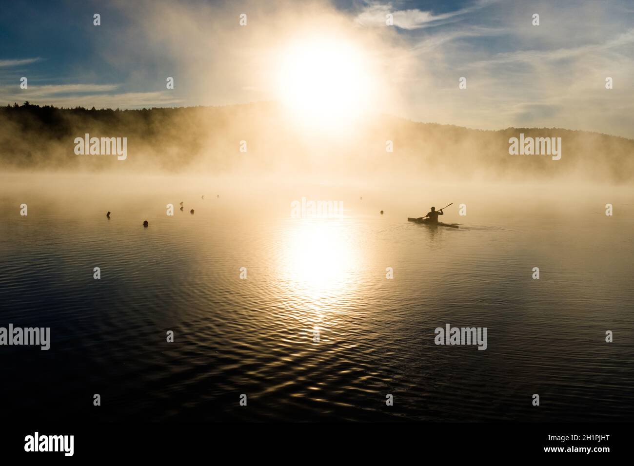 Kayak silhouetted dal sole nascente sul lago Iroquois in Vermont, USA, New England, in una mattinata di settembre nebbiosa. Foto Stock