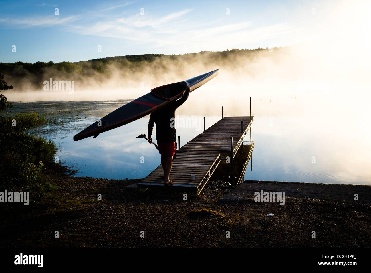 Kayak silhouetted dal sole nascente sul lago Iroquois in Vermont, USA, New England, in una mattinata di settembre nebbiosa. Foto Stock