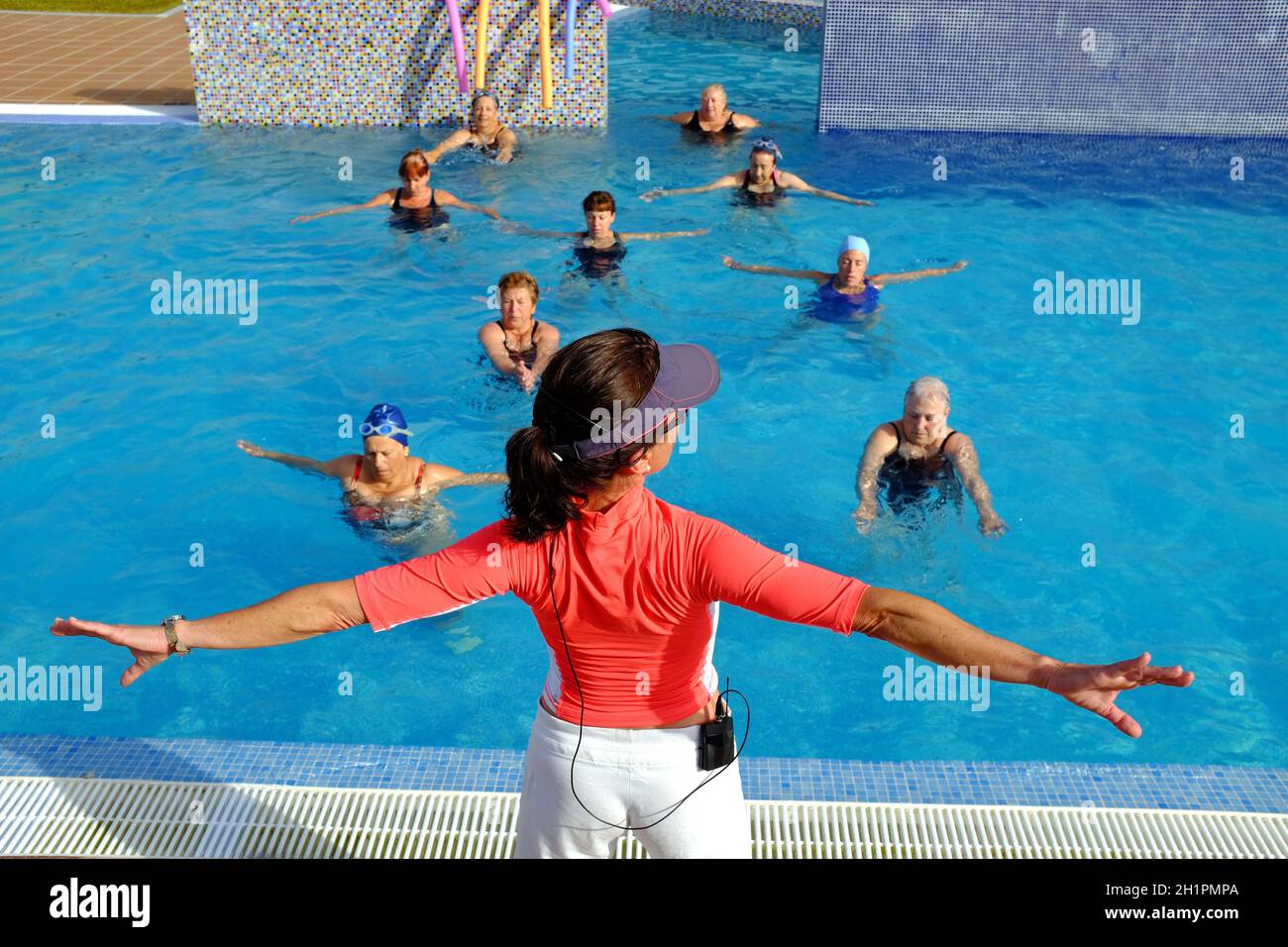Primo piano della vista posteriore dell'allenatore di fitness durante una sessione di classe di salute senior nella piscina all'aperto. Foto Stock