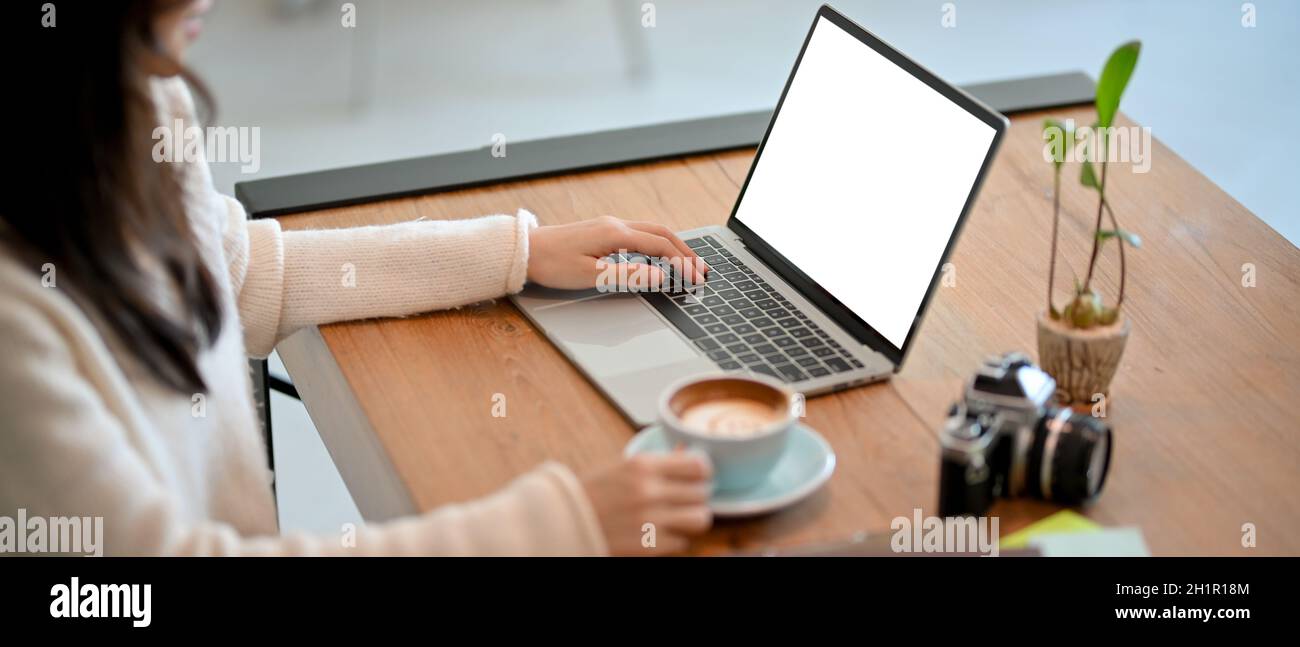 Primo piano di una fotografo freelance femminile o di un blogger di caffè selezionando una fotografia, lavorando, e scrivendo una recensione di un caffè sul suo computer portatile in un caffè Foto Stock