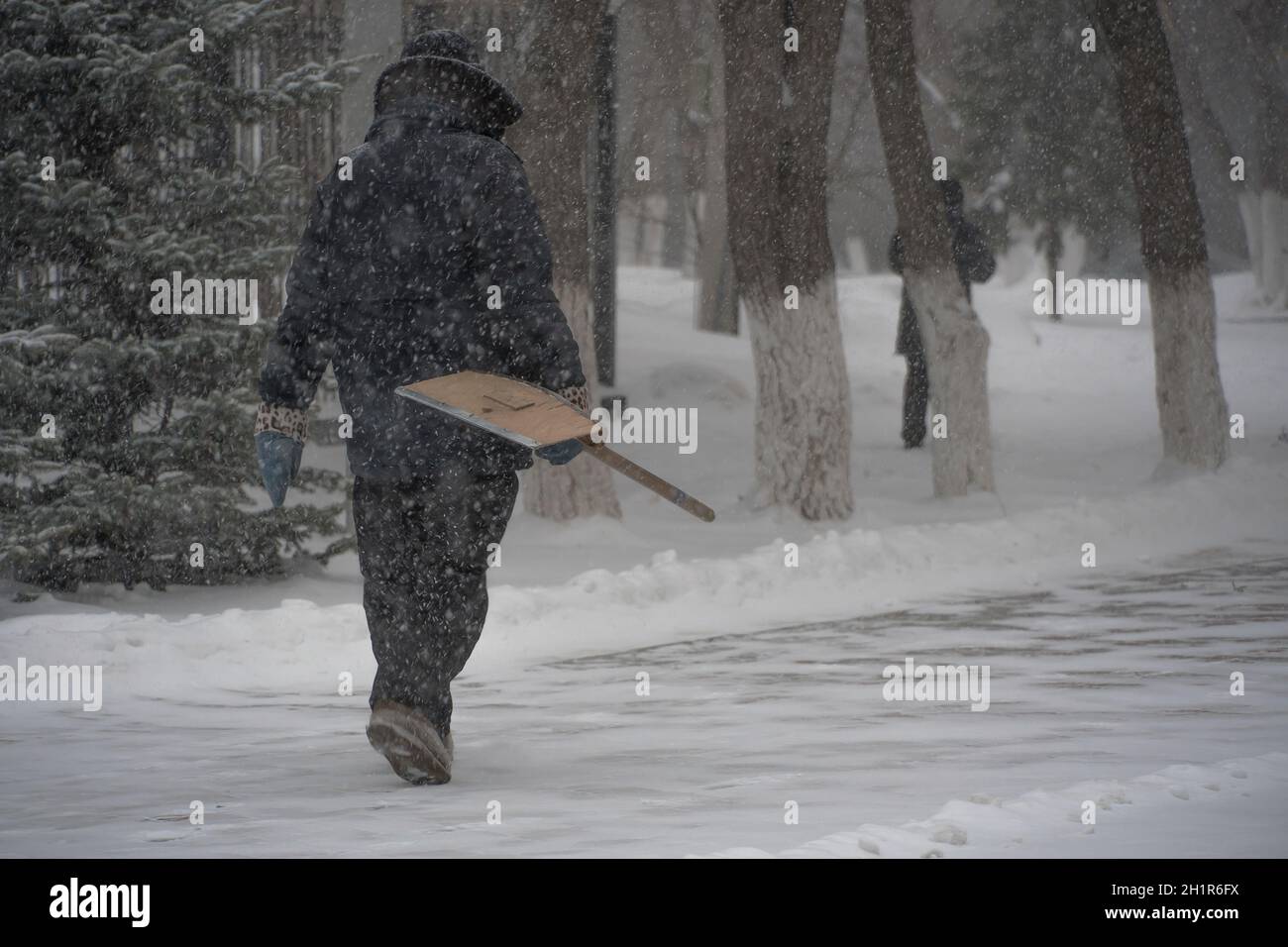 Un uomo che lavora al servizio comunale con una pala da neve cammina lungo la strada in una tempesta, una bizzarda o una nevicata in inverno in caso di maltempo nella città.E. Foto Stock