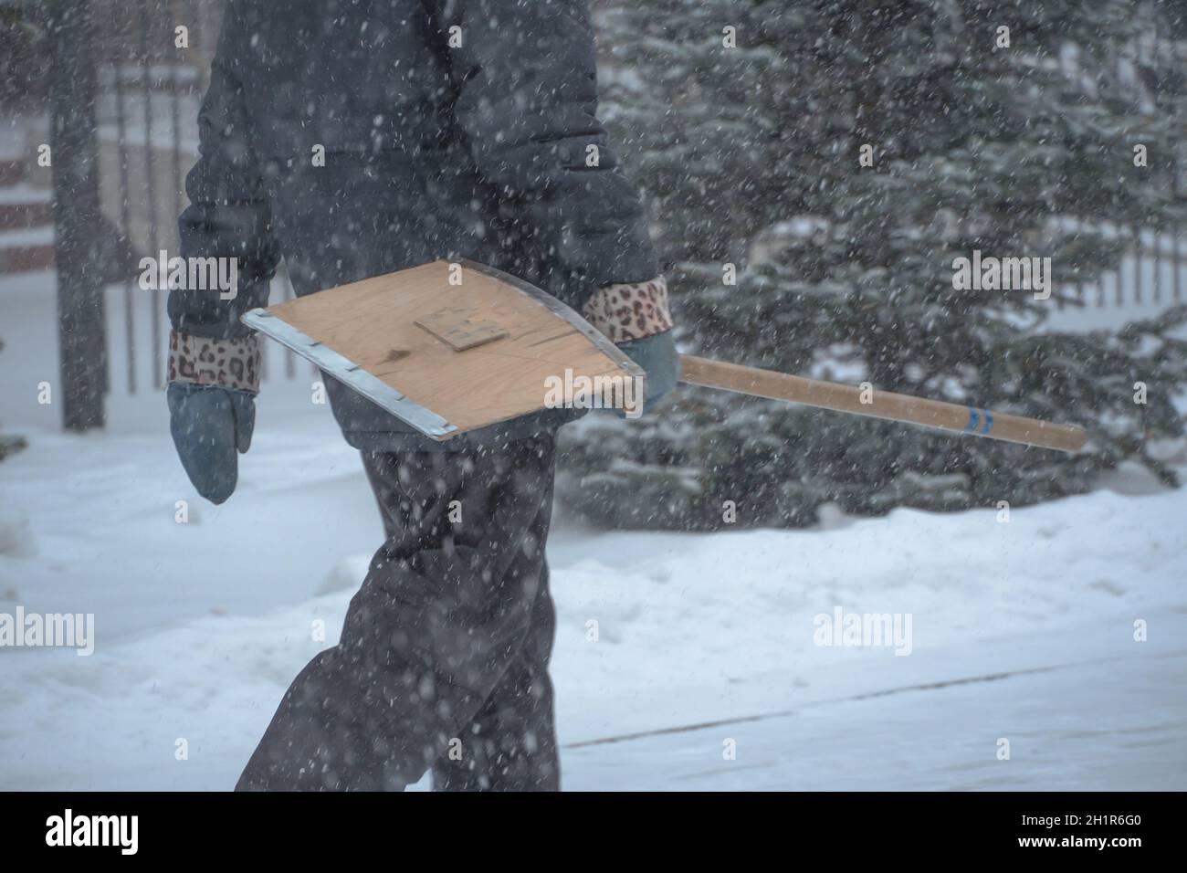 Un uomo che lavora al servizio comunale con una pala da neve cammina lungo la strada in una tempesta, una bizzarda o una nevicata in inverno in caso di maltempo nella città.E. Foto Stock