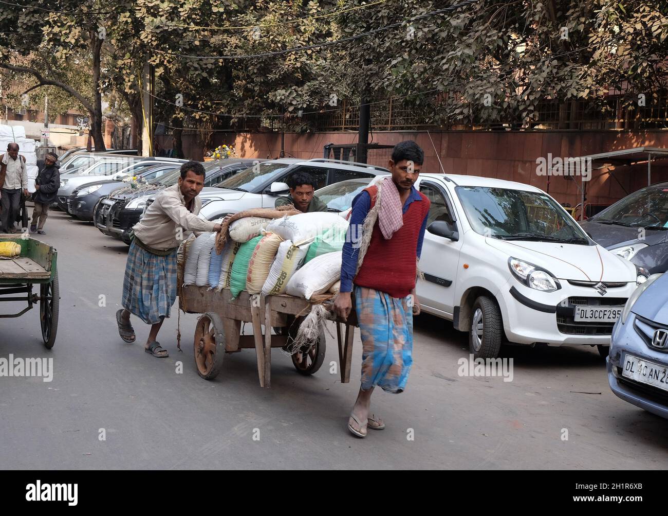 Gli indiani che lavorano duramente spingono carichi pesanti attraverso le strade di Delhi, India Foto Stock