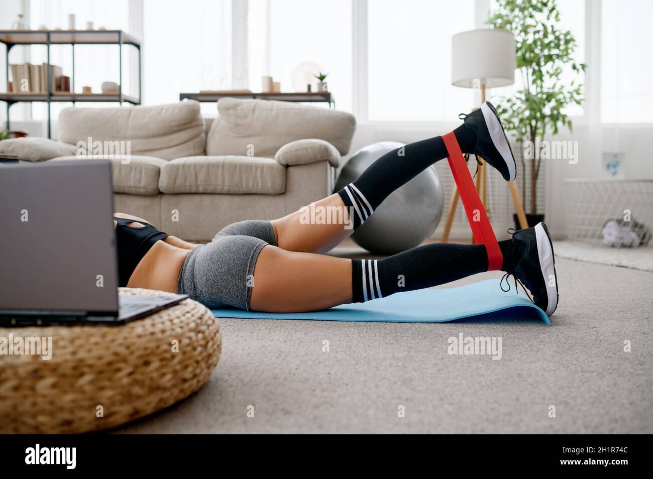 Donna sdraiata sul pavimento, allenamento fitness online. Donna in abbigliamento sportivo, allenamento sportivo su internet, camera interna su sfondo Foto Stock