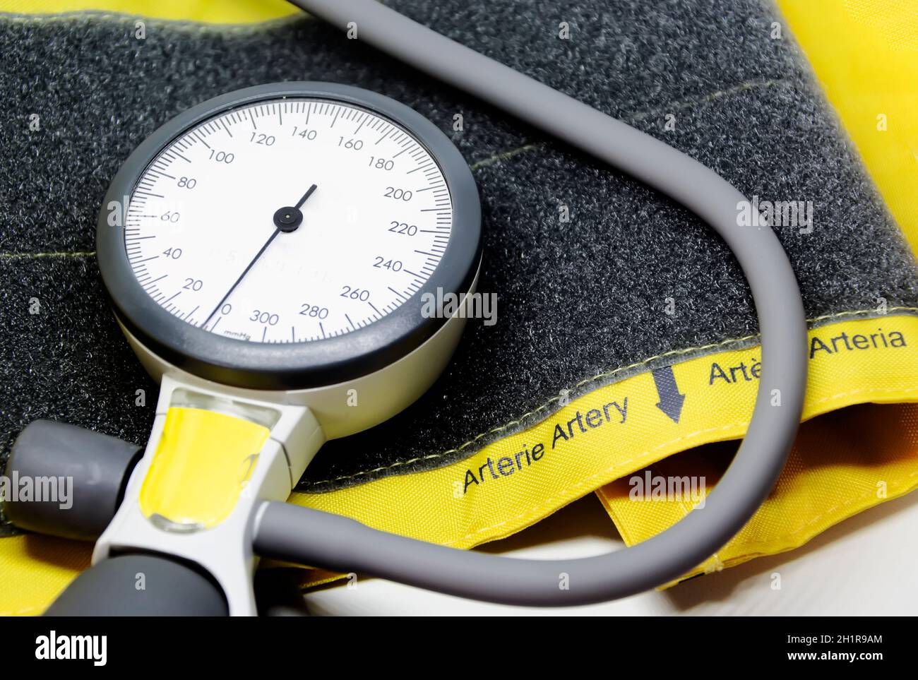 uno sfigmomanometro portatile poggiato su un bracciale giallo per adulti con chiusura in velcro. Strumento per la misurazione della pressione sanguigna. Scala graduata con p Foto Stock