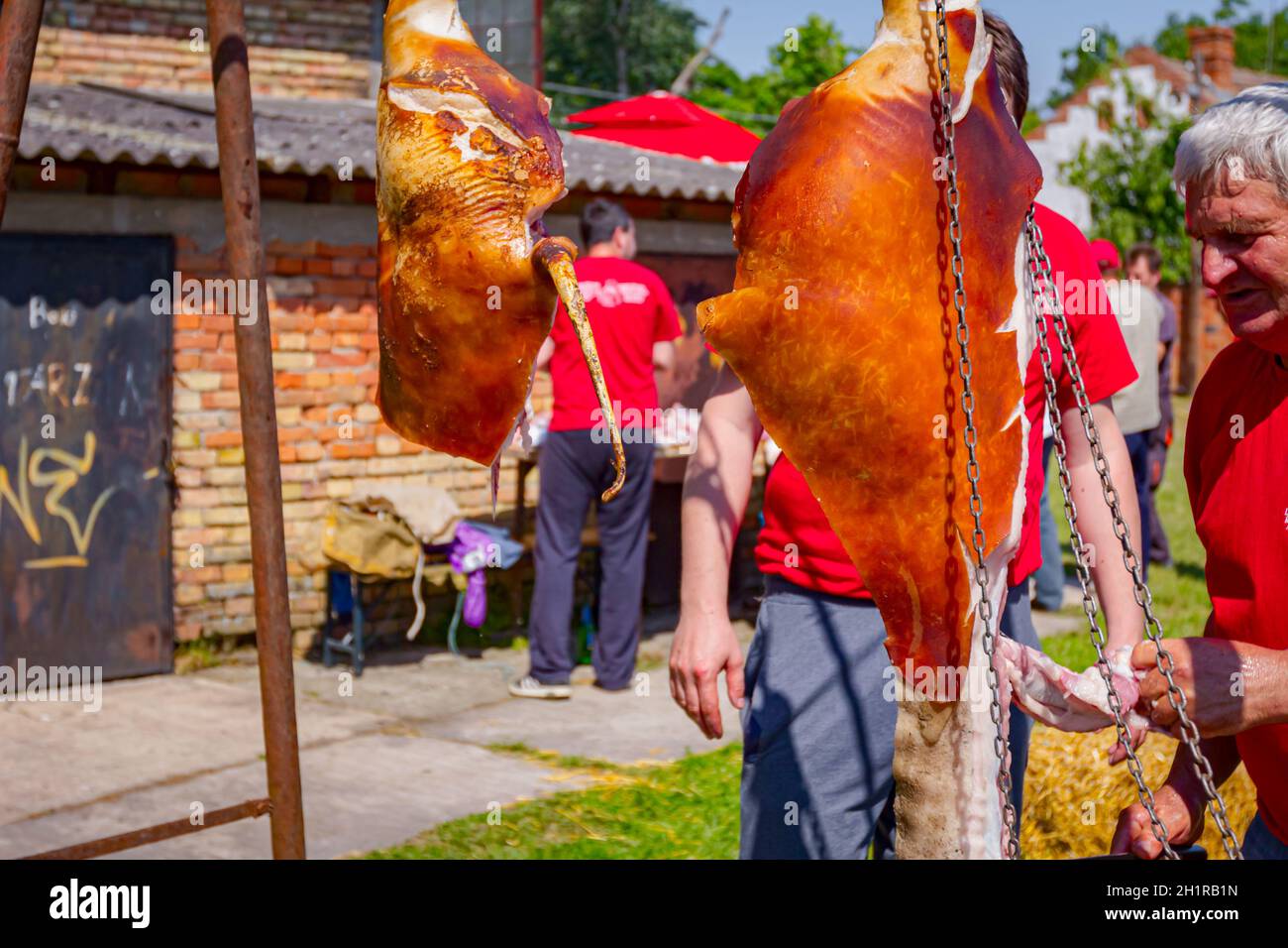Aradac, Vojvodina, Serbia - 21 maggio 2016: Due prosciutti di maiale crudi sono appesi sopra nel cortile del villaggio, macellaio sta tagliando la carne. Foto Stock