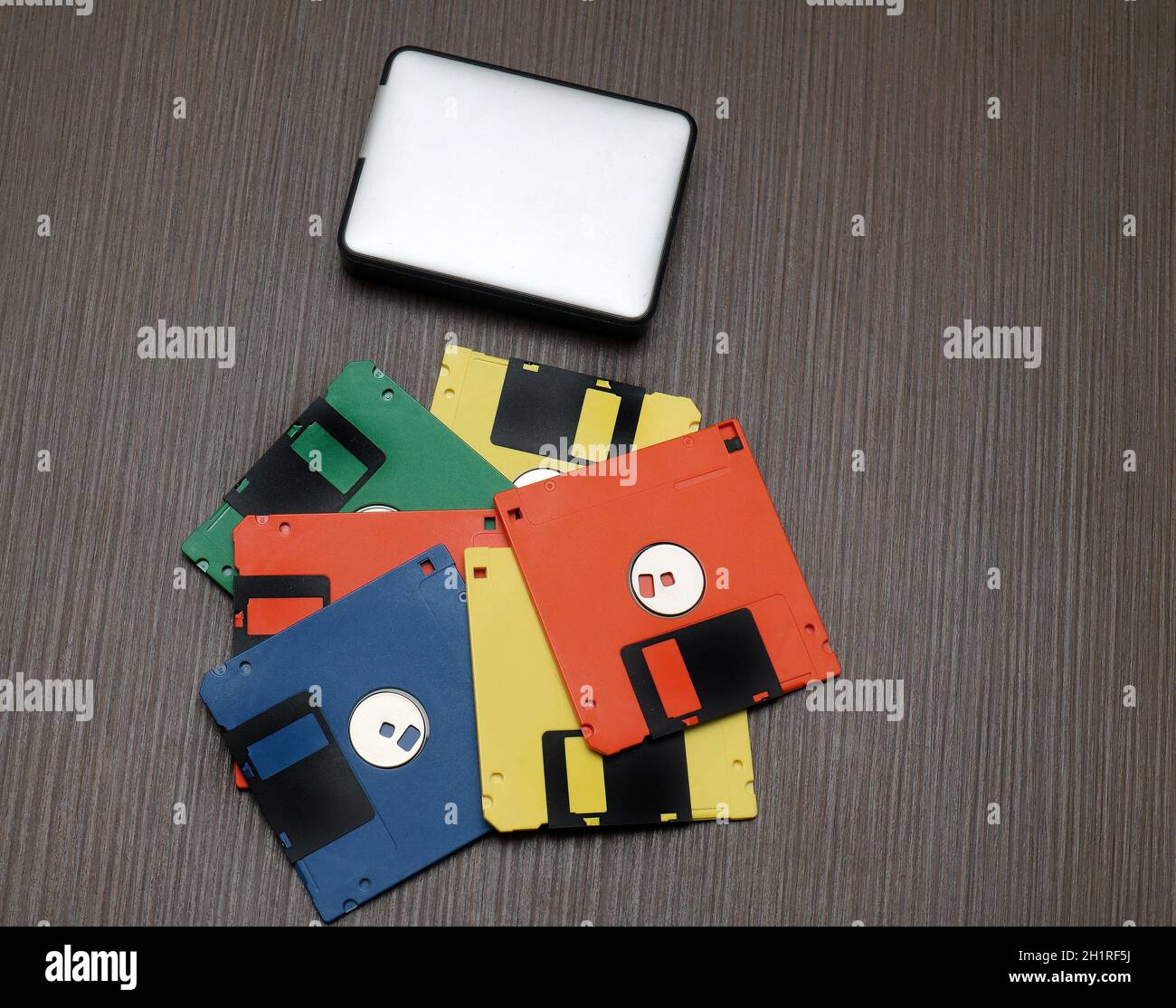 Vecchi floppy disk retrò colorati e moderno disco rigido esterno su tavolo di legno Foto Stock