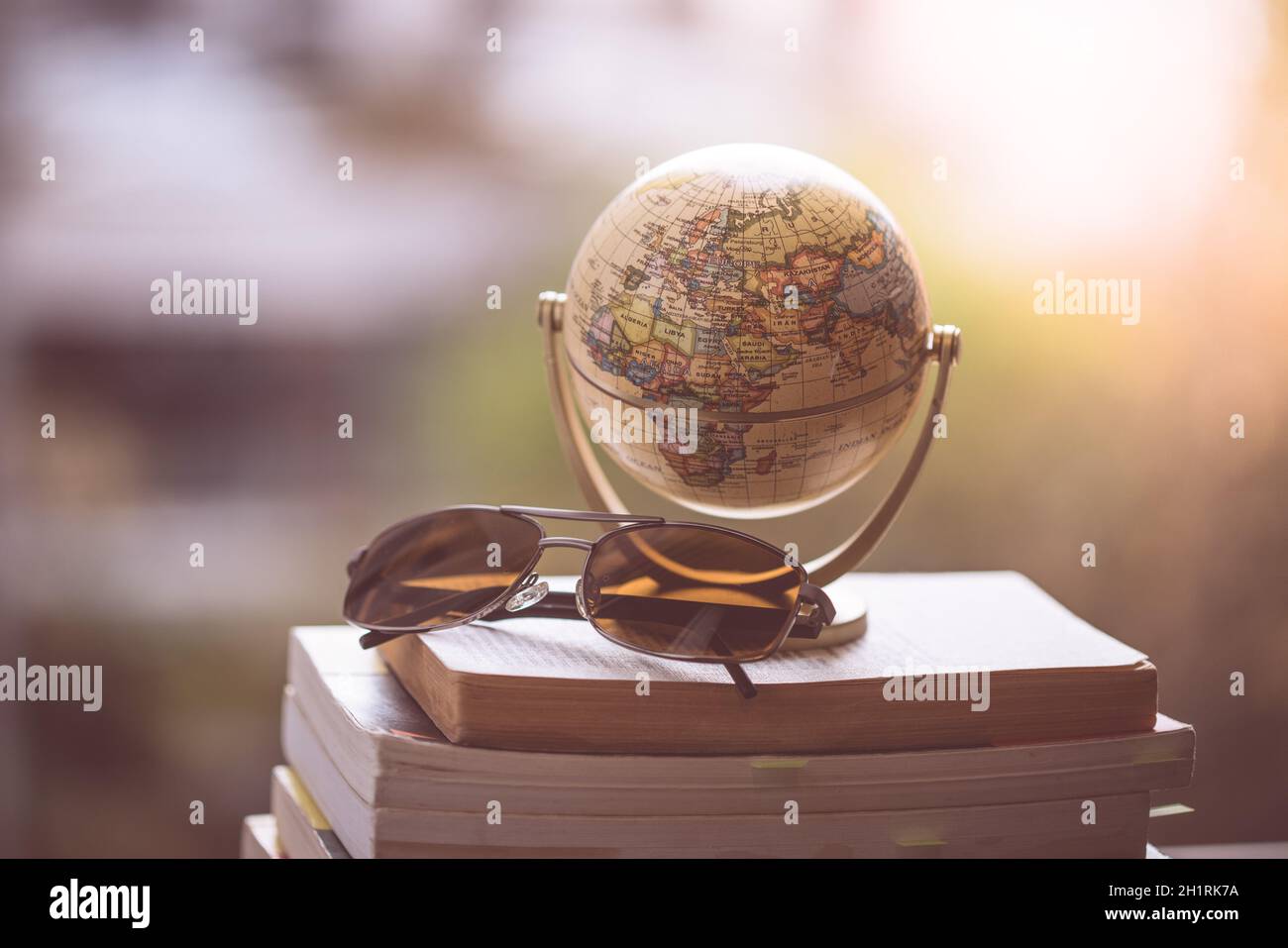 Globo in miniatura del modello e occhiali da sole giacente su una pila di libri. Simbolo per il viaggio. Foto Stock