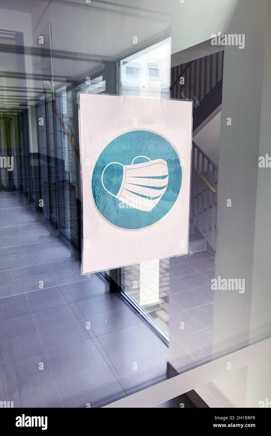 Cartello con la maschera Corona nell'edificio scolastico su una porta di vetro, si prega di indossare la maschera Foto Stock