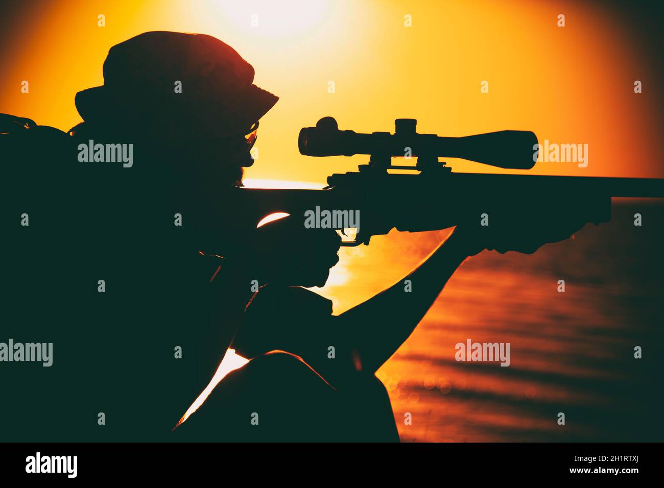 Il cecchino della squadra di Commando, lo sparatutto dell'esercito con forze speciali che punta, spara il fucile da cecchino mentre si siede sul mare o sulla riva dell'oceano durante il tramonto. Costa o confine gua Foto Stock