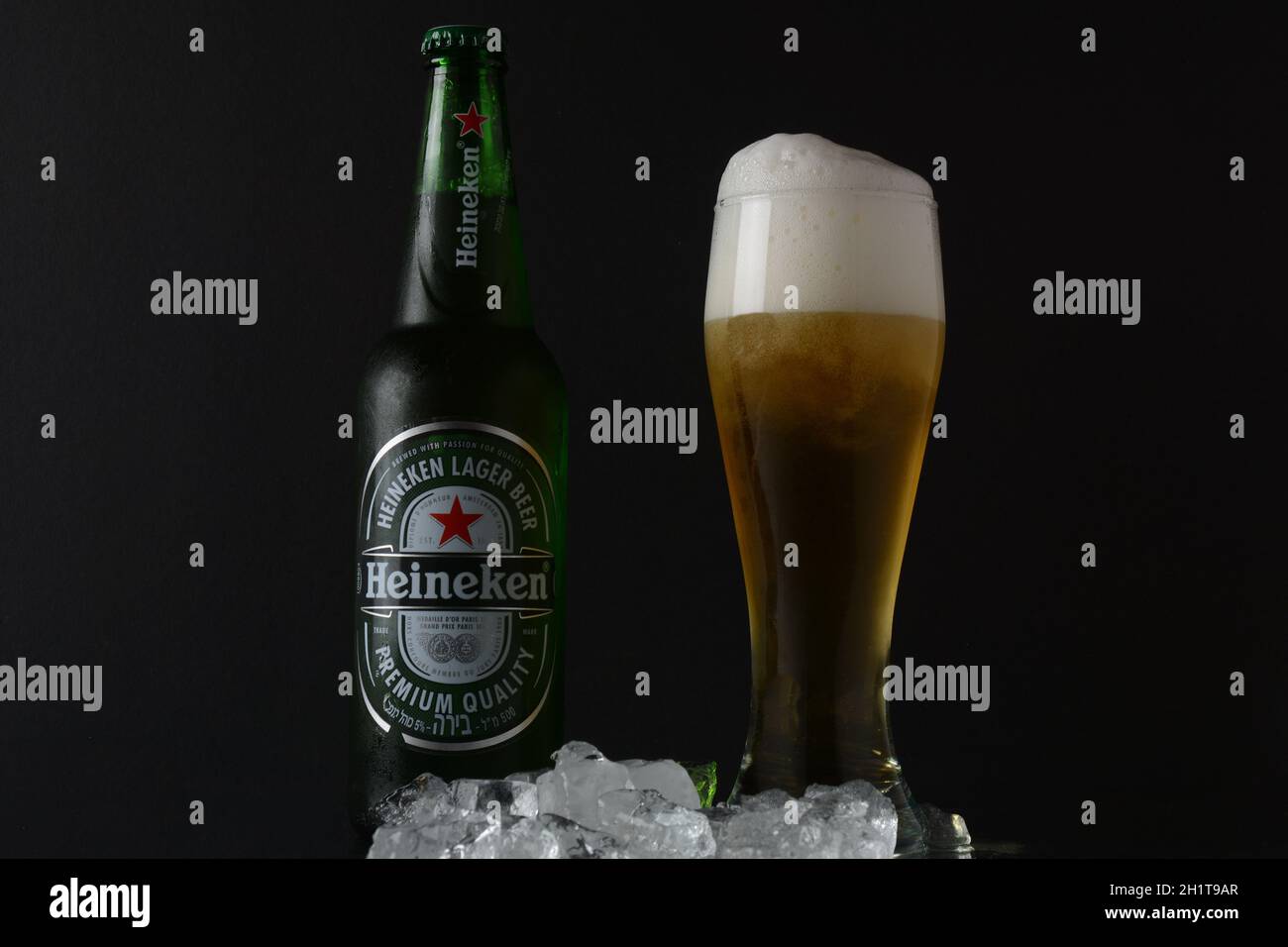 NETANYA, ISRAELE - 01 luglio 2020: Bicchiere freddo di birra e una bottiglia di vetro di birra Heineken su sfondo nero con cubetti di ghiaccio. Heineken N.V. è un olandese b Foto Stock