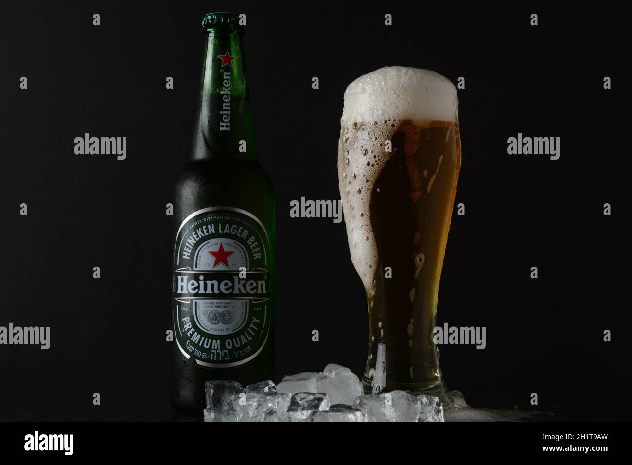 NETANYA, ISRAELE - 01 luglio 2020: Bicchiere freddo di birra e una bottiglia di vetro di birra Heineken su sfondo nero con cubetti di ghiaccio. Heineken N.V. è un olandese b Foto Stock